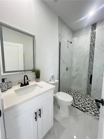 Bathroom featuring marble finish flooring, toilet, a marble finish shower, and vanity