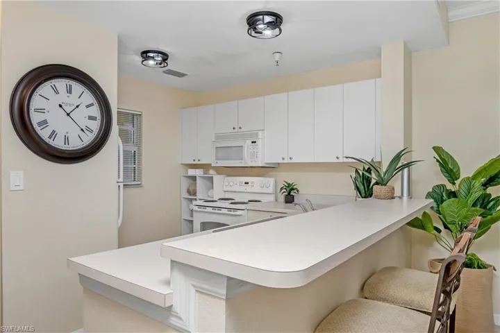 Kitchen with white cabinetry, crown molding, white appliances, a kitchen bar, and kitchen peninsula