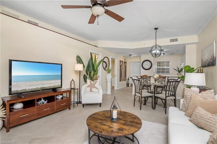 Tiled living room with ceiling fan with notable chandelier and crown molding