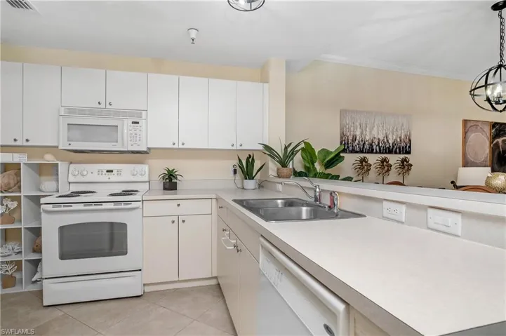 Kitchen with light tile patterned flooring, white cabinetry, white appliances, decorative light fixtures, and sink