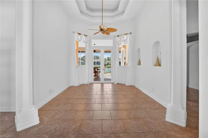 Tiled entryway featuring a tray ceiling, french doors, a ceiling fan, a water view, and decorative columns