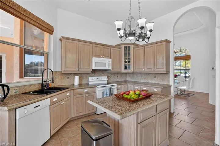 Kitchen with light brown cabinets, white appliances, glass insert cabinets, light tile patterned flooring, and hanging light fixtures