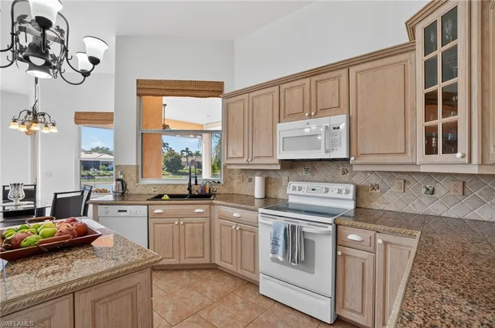 Kitchen with white appliances, light brown cabinets, decorative backsplash, a chandelier, and glass insert cabinets