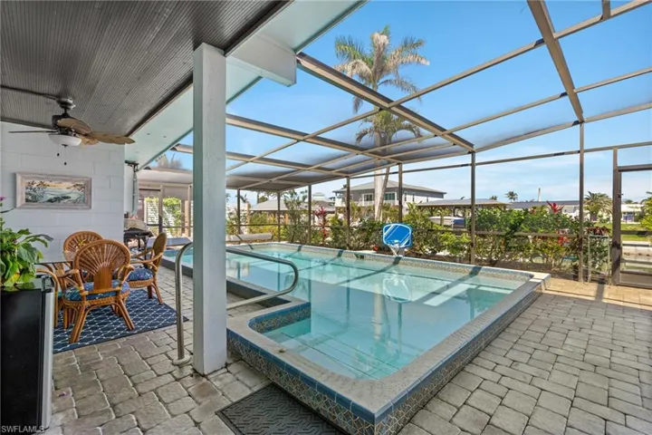 Outdoor pool featuring glass enclosure, a patio area, a ceiling fan, and a hot tub virtually enhanced image