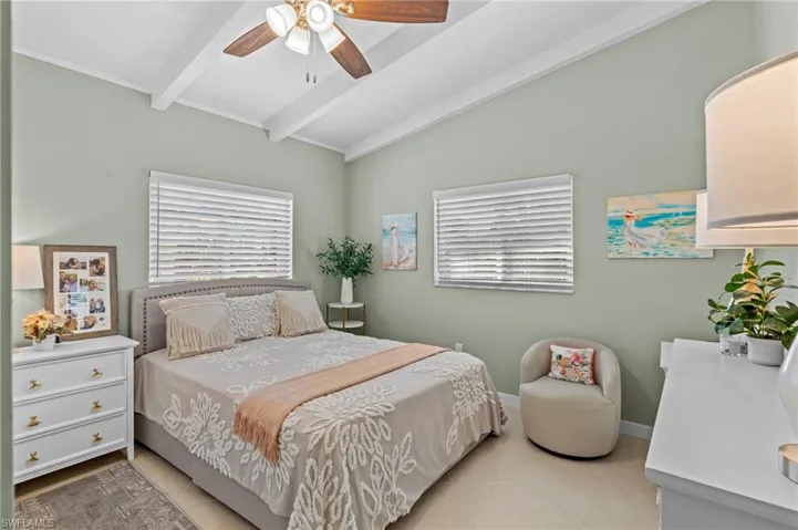 Tiled bedroom with a ceiling fan, lofted ceiling with beams, and baseboards