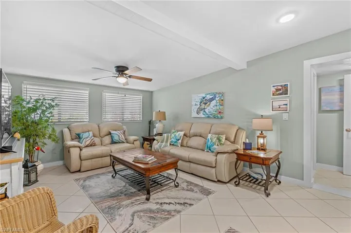 Living area featuring a ceiling fan, baseboards, beam ceiling, and light tile patterned flooring