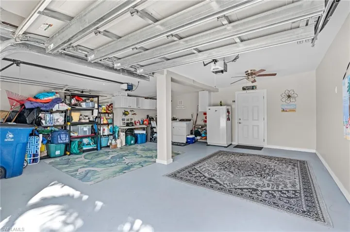 Garage featuring baseboards, a ceiling fan, freestanding refrigerator, and a garage door opener virtually enhanced image