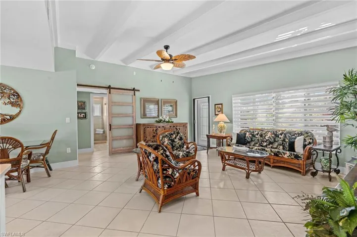 Living area with beam ceiling, light tile patterned floors, a barn door, ceiling fan, and baseboards