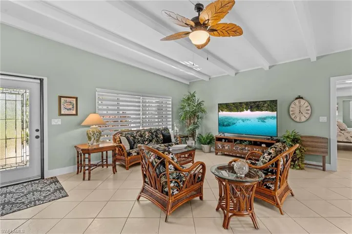 Tiled living area featuring vaulted ceiling with beams, ceiling fan, and baseboards