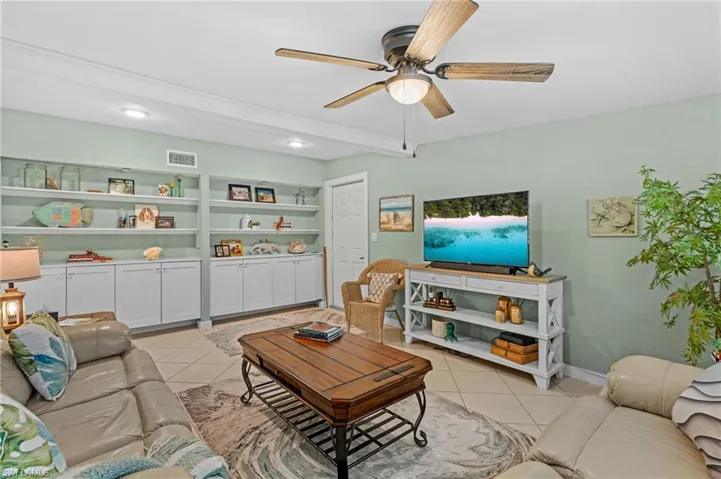 Living room with built in shelves, light tile patterned floors, visible vents, ceiling fan, and baseboards