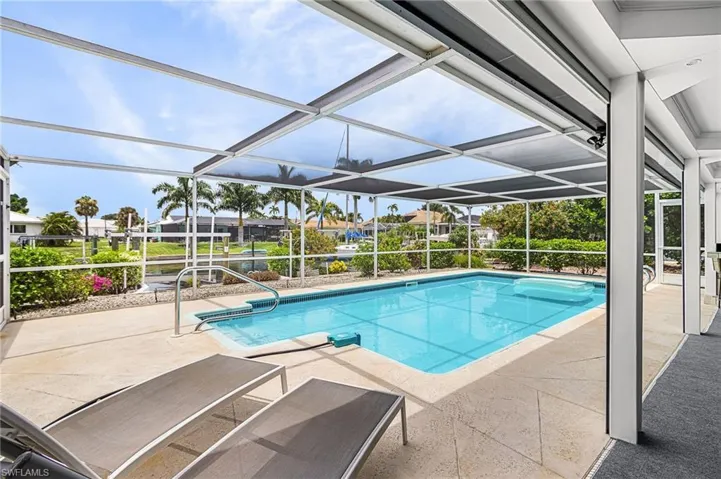 Screened heated pool featuring integrated steps and handrails, complemented by a textured concrete deck.