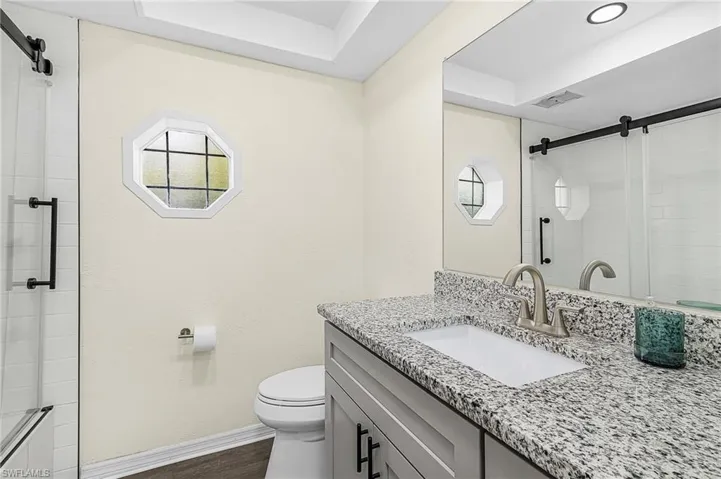 Bathroom with granite countertop, wood-finish flooring.
