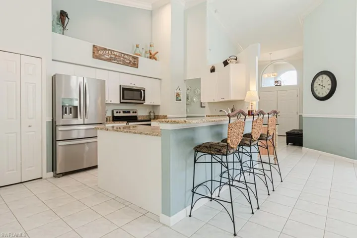 Kitchen featuring light stone countertops, stainless steel appliances, crown molding, a breakfast bar area, and white cabinets