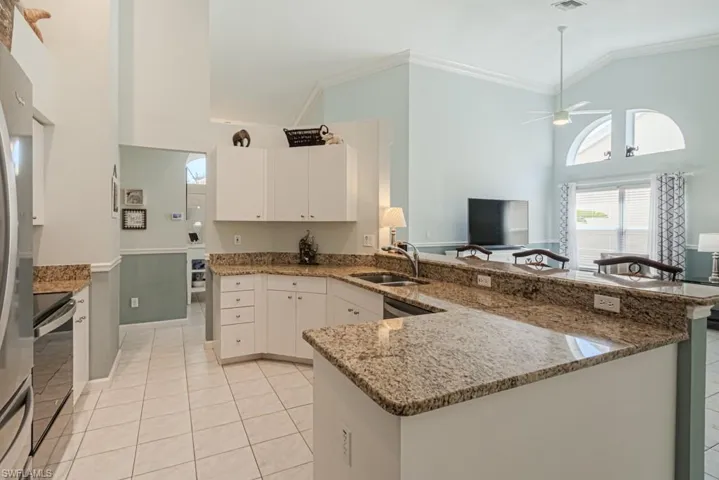 Kitchen with high vaulted ceiling, white cabinets, sink, ceiling fan, and kitchen peninsula