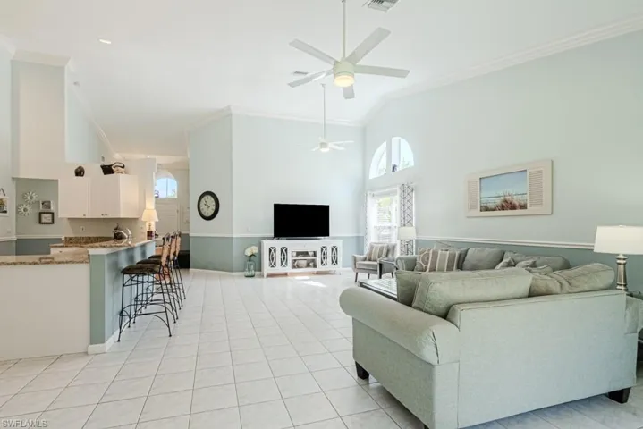 Living room featuring high vaulted ceiling, ceiling fan, ornamental molding, and light tile patterned flooring