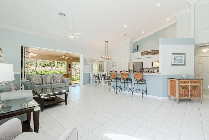 Living room with ceiling fan with notable chandelier, high vaulted ceiling, ornamental molding, and light tile patterned flooring
