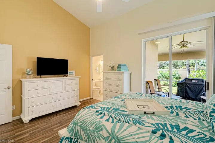Bedroom with dark hardwood / wood-style floors, ceiling fan, high vaulted ceiling, and ensuite bath