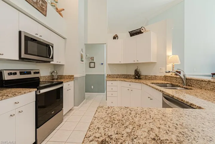 Kitchen with light stone countertops, sink, stainless steel appliances, white cabinets, and light tile patterned flooring