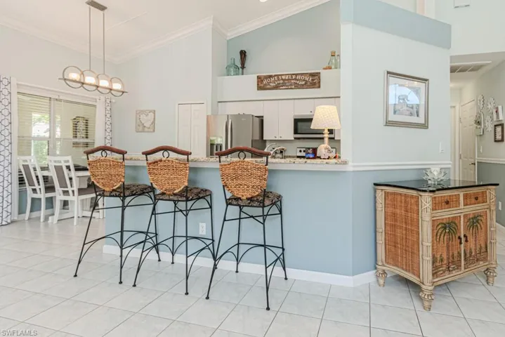 Kitchen with hanging light fixtures, ornamental molding, appliances with stainless steel finishes, light tile patterned flooring, and white cabinetry