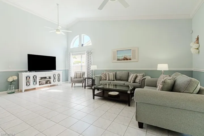Living room with ceiling fan, light tile patterned flooring, high vaulted ceiling, and ornamental molding