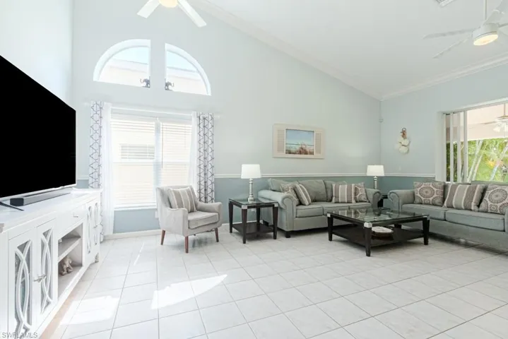 Tiled living room featuring ceiling fan, plenty of natural light, high vaulted ceiling, and ornamental molding