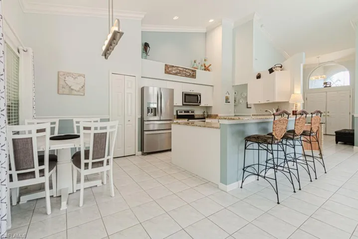 Kitchen with a breakfast bar, kitchen peninsula, light tile patterned flooring, white cabinetry, and stainless steel appliances