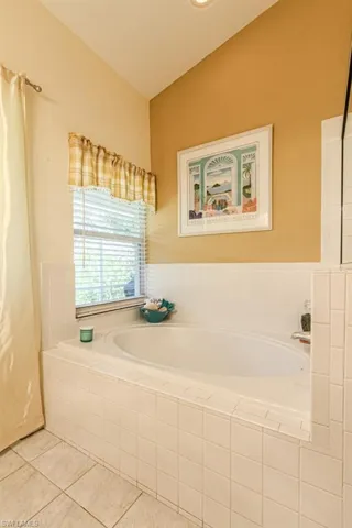 Bathroom featuring tile patterned floors, vaulted ceiling, and tiled tub