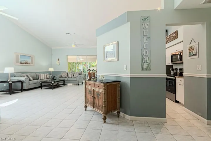 Living room featuring crown molding, ceiling fan, light tile patterned flooring, and vaulted ceiling