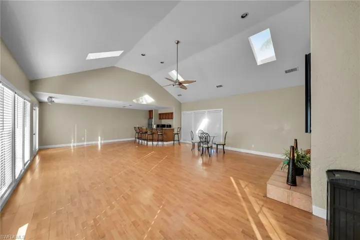 Living room featuring hardwood / wood-style floors, a skylight, high vaulted ceiling, and ceiling fan