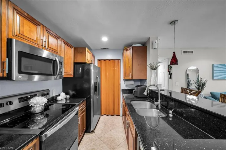 Kitchen featuring sink, dark stone counters, hanging light fixtures, light tile patterned floors, and stainless steel appliances