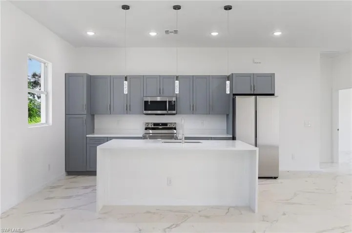 Kitchen featuring gray cabinetry, stainless steel appliances, an island with sink, and pendant lighting