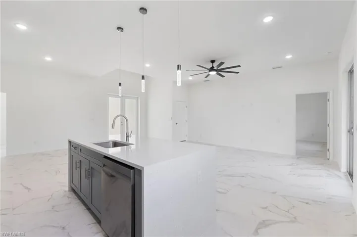 Kitchen with decorative light fixtures, a center island with sink, dishwasher, sink, and ceiling fan