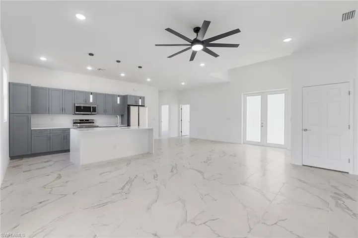Kitchen with decorative light fixtures, an island with sink, stainless steel appliances, gray cabinets, and ceiling fan