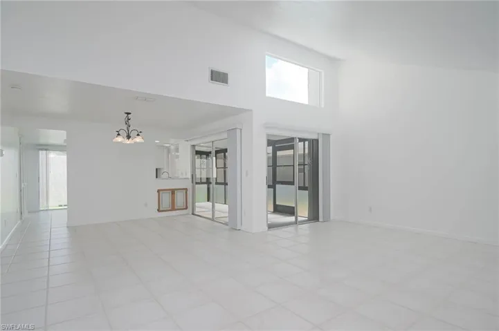 Unfurnished living room featuring a healthy amount of sunlight, a high ceiling, light tile patterned floors, and a chandelier
