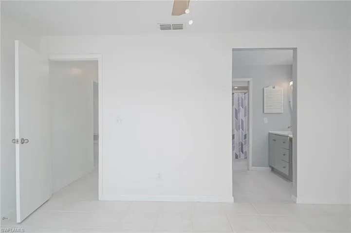 Unfurnished bedroom featuring ensuite bath, ceiling fan, and light tile patterned flooring