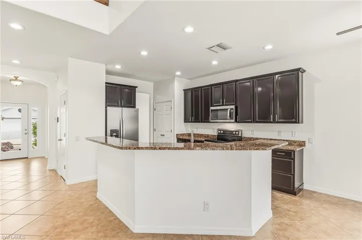 Kitchen with dark stone countertops, arched walkways, stainless steel appliances, light tile patterned floors, and recessed lighting