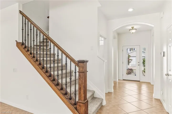 Foyer featuring light tile patterned flooring, arched walkways, stairs, and recessed lighting