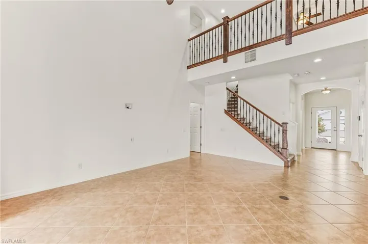 Unfurnished living room featuring recessed lighting, arched walkways, stairway, a towering ceiling, and light tile patterned flooring