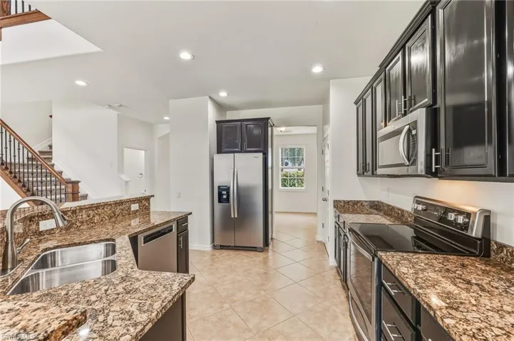 Kitchen with appliances with stainless steel finishes, dark stone countertops, recessed lighting, light tile patterned floors, and dark cabinets