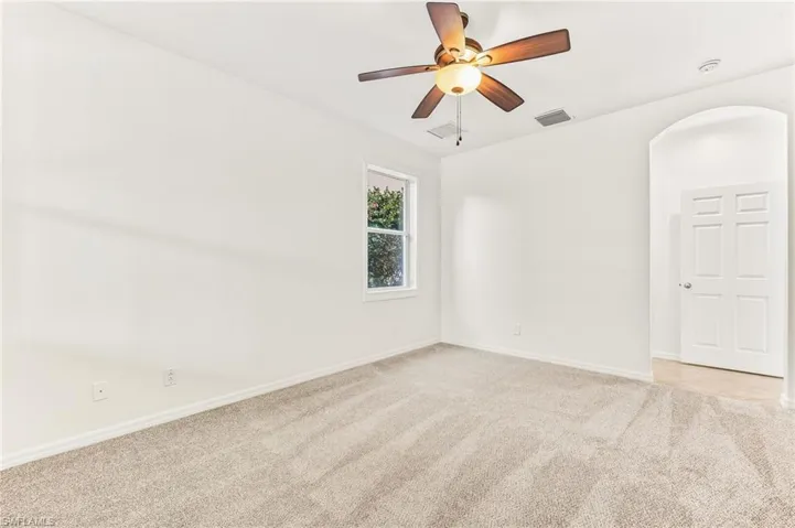 Empty room featuring light colored carpet, ceiling fan, and arched walkways