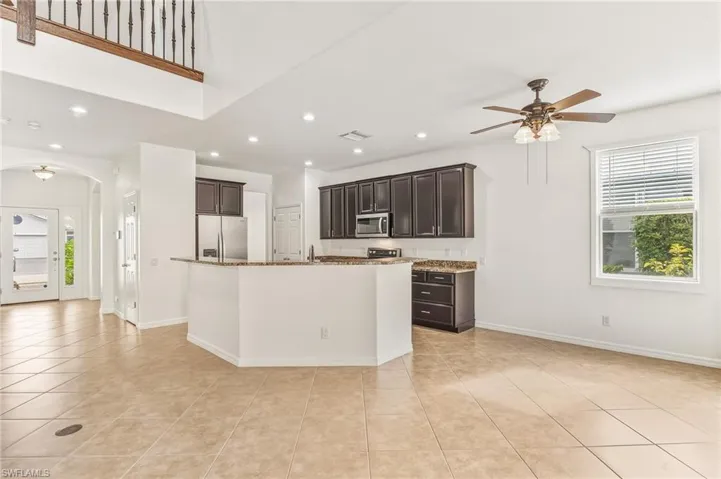 Kitchen featuring arched walkways, dark brown cabinetry, appliances with stainless steel finishes, light stone counters, and ceiling fan