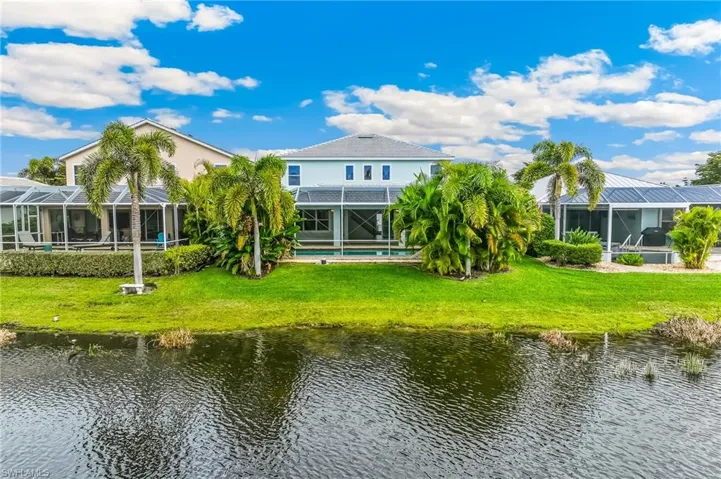 Back of house featuring a sunroom, a water view, and a lawn