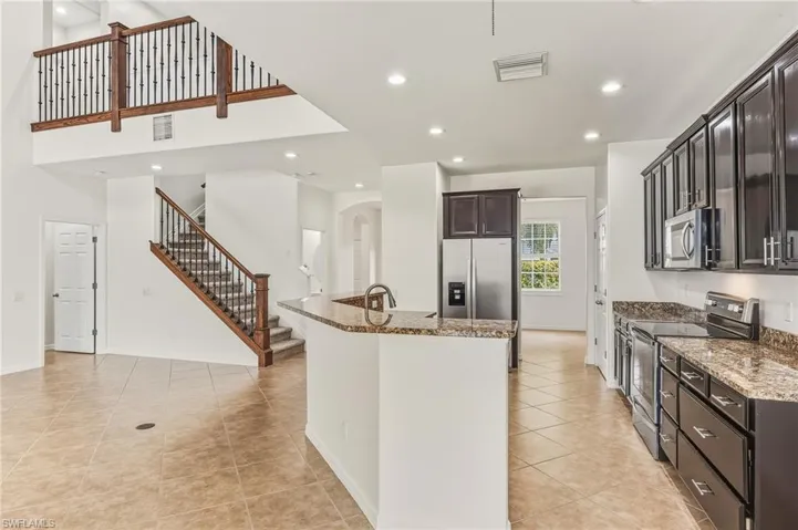 Kitchen featuring stainless steel appliances, light tile patterned flooring, light stone countertops, recessed lighting, and arched walkways