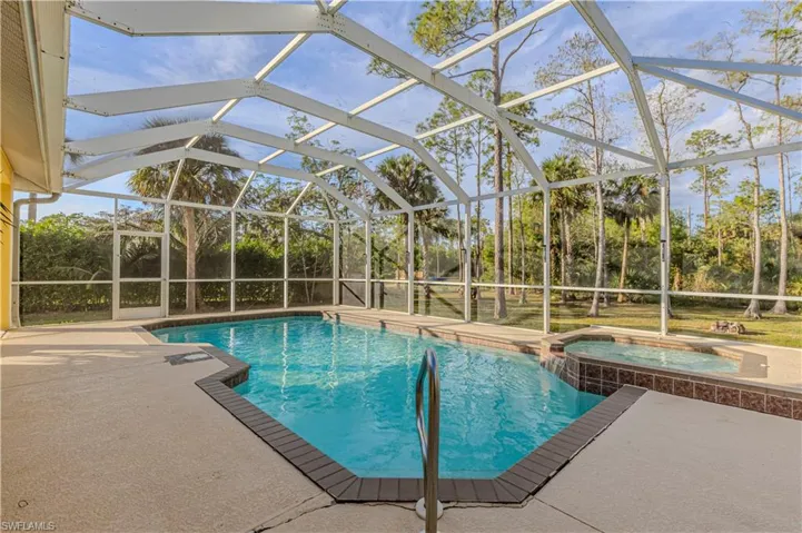 View of swimming pool featuring glass enclosure, an in ground hot tub, and a patio