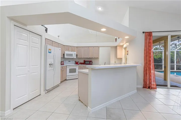 Kitchen with light brown cabinets, lofted ceiling, white appliances, light tile patterned flooring, and kitchen peninsula