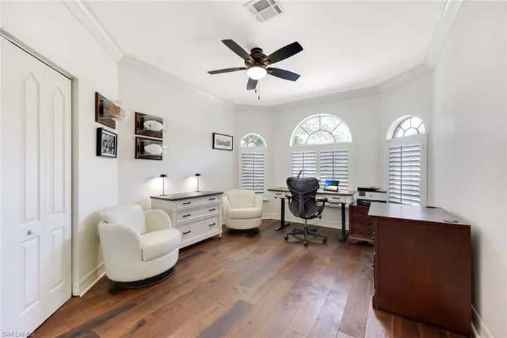 Spacious den with elegant wood flooring and detailed crown molding, creating a warm and inviting atmosphere.