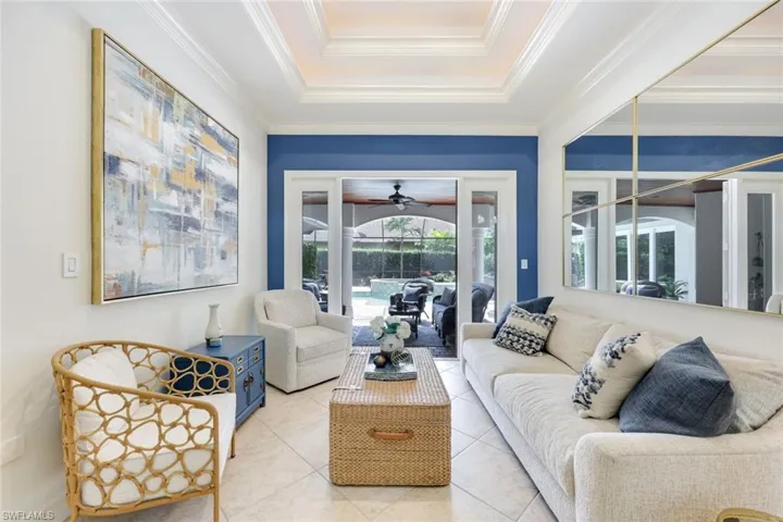 Well-appointed living room featuring attractive tile flooring, tray ceilings, crown molding, and charming French doors that offer a delightful connection to the outdoors.