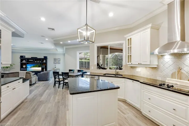 Kitchen featuring pendant lighting, wall chimney range hood, tasteful backsplash, ornamental molding, and dark stone countertops