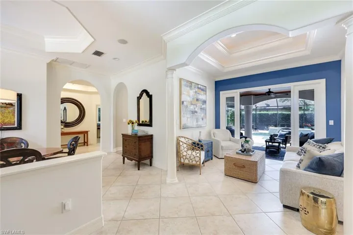 Well-appointed living room featuring attractive tile flooring, tray ceilings, crown molding, and charming French doors that offer a delightful connection to the outdoors.