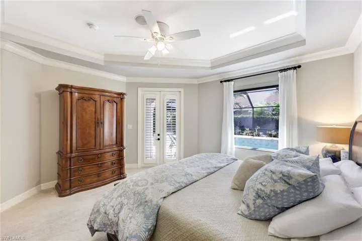 Spacious and elegant primary bedroom featuring attractive crown molding, plush carpeting on the floor, and a beautifully designed tray ceiling.